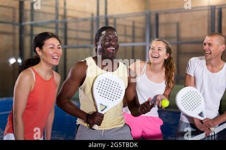 Eine Gruppe fröhlicher Paddle-Tennisspieler, die sich auf einem geschlossenen Platz unterhalten Stockfoto