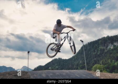 Ein Mann, der durch die Luft fliegt, während er mit dem Fahrrad eine unbefestigte Straße entlang fährt Stockfoto