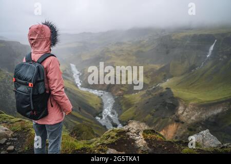 Frau in Fliederjacke mit Rucksack, die das isländische Hochland und den Fluss Fossa in der Nähe des Haifoss Wasserfalls in Island genießt Stockfoto