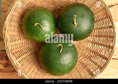Drei reife saftige Wassermelonen in einer Strohschale, Nahaufnahme, auf einem Holztisch, Draufsicht. Stockfoto