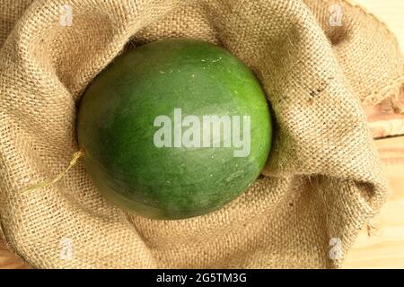 Eine süße, dunkelgrüne, saftige Wassermelone auf Jutestoff, Nahaufnahme, auf einem Holztisch, Draufsicht. Stockfoto