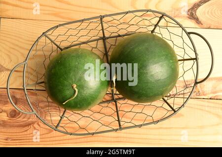 Zwei reife Bio-Wassermelonen in einem Metallkorb, Nahaufnahme, auf einem Holztisch, Draufsicht. Stockfoto