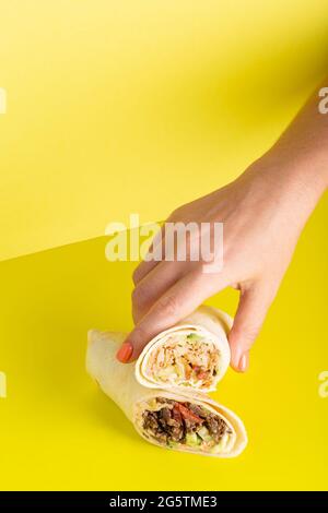 Die Hand nimmt Dönerrolle Shawarma mit Huhn und Gemüse auf gelb Stockfoto