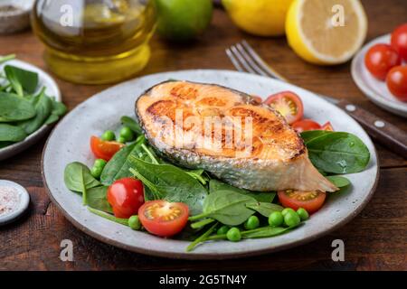 Gebratenes Lachssteak serviert mit grünem Salat aus Babyspinat, Kirschtomaten und Erbsen. Gesunde Mahlzeit Stockfoto