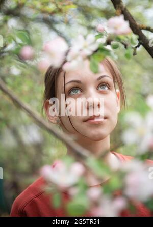 Ein junges Mädchen in einem blühenden Garten blickt auf blühende Bäume Stockfoto