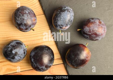 Mehrere organische schwarze Pflaumen auf einer Schiefertafel, Nahaufnahme, auf einem Holztisch, Draufsicht. Stockfoto