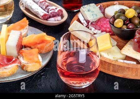 Rosenwein mit Wurstwaren, Käse und Lachs-Sandwiches. Spanische Tapas. Jamon, Fuet, Ziege und Blauschimmelkäse sowie Oliven auf schwarzem Hintergrund Stockfoto