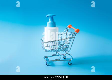 Weiße Plastikflasche mit Spender in einem Mini-Supermarkt-Trolley auf hellblauem Hintergrund. Einkaufskonzept. Stockfoto