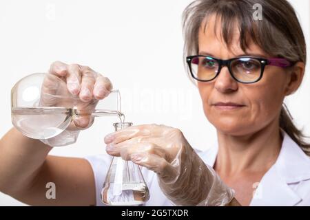 Frau in einem Labormantel, die Flüssigkeit in einen Laborkolben gießt Stockfoto