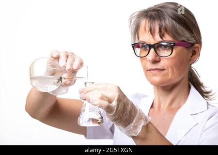 Frau in einem Labormantel, die Flüssigkeit in einen Laborkolben gießt Stockfoto