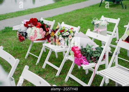 Blumensträuße auf weißen Holzstühlen bei der Zeremonie am Ausgang. Stockfoto
