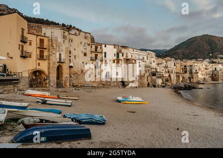 Schöner alter Hafen mit hölzernen Fischerbooten, bunten Steinhäusern am Wasser und Sandstrand in Cefalu, Sizilien, Italien. Stockfoto