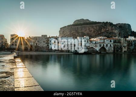 Sonnenaufgang im Hafen von Cefalu, Sizilien, Italien, Altstadt Panoramablick mit bunten Häusern am Wasser, Meer und La Rocca Klippe.attraktiver Sommer Stockfoto