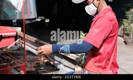 Mann mit rotem Hemd Kochen Bar B Q auf Grill Klong Toey Market Großhandel Wet Market Bangkok Thailand größte Lebensmittelverteilzentrum in Südostasien Stockfoto