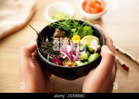 Ein Mann hält einen Poke-Salat mit Rindfleisch in einer Schüssel in den Händen. Zutaten Rindfleisch, Nameko-Pilze, Kirschtomaten, Reis, Gurke, Rote Zwiebel, Sesam Stockfoto