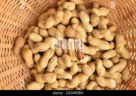 Reife, ungeschälte Erdnüsse in einem Weidenkorb aus Stroh, Nahaufnahme, Draufsicht. Stockfoto