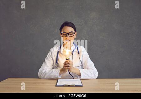 Porträt einer Ärztin, die sich die beleuchtete Idee einer Glühbirne im Studio ansieht Stockfoto
