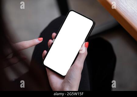 Draufsicht Mockup-Bild einer Frau, die ein schwarzes Mobiltelefon mit leerem weißen Bildschirm hält, während sie im Café sitzt. Stockfoto