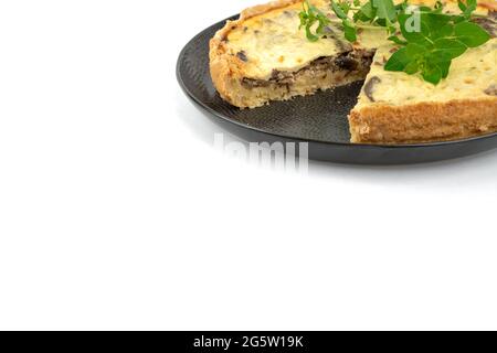 Nahaufnahme breites Studio-Shot von frisch gebackenen gelben französischen salzigen Kuchen oder Quiche, mit Pilzen und grüner Minze, auf einem schwarzen Design-Teller, isoliert auf Whi Stockfoto