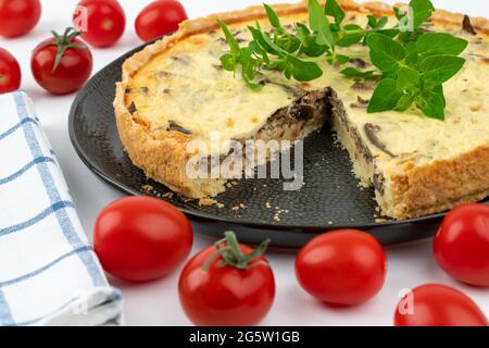 Nahaufnahme breite Studio-Aufnahme von frisch gebackenen gelben Französisch salzigen Kuchen, oder Quiche mit Pilzen, rote Kirschtomaten, grüne Minze und Küchentuch, auf einem Stockfoto