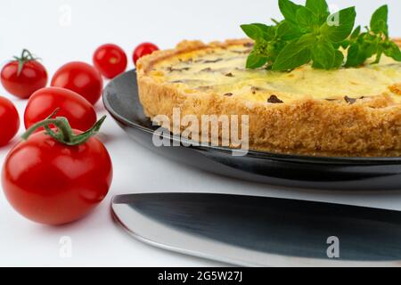 Nahaufnahme breite Studio-Aufnahme von frisch gebackenen gelben Französisch salzigen Kuchen oder Quiche, mit Pilzen, rote Kirschtomaten, auf einem schwarzen Design-Platte isoliert o Stockfoto