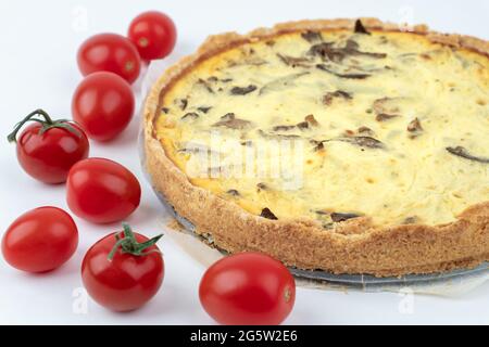 Nahaufnahme von frisch gebackenen gelben französischen salzigen Kuchen oder Quiche mit Pilzen, roten Kirschtomaten, noch auf Backpapier, isoliert auf weiß Stockfoto