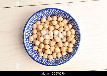 Bio-Kichererbsen in einer Keramikuntertasse, Nahaufnahme, auf einem weißen Holztisch, Draufsicht. Stockfoto