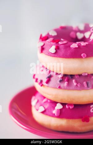 Leuchtend rosa süße leckere Donuts mit Streuseln in Form von Herzen liegen auf einer rosa Untertasse. Ein romantisches Geschenk zum Valentinstag. Süßigkeiten für Th Stockfoto