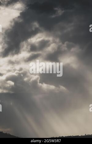 Dicke, stürmische Wolken über den Bergen mit intensiven Sonnenstrahlen, die durch die Berge ragen, und kontrastreicher Lichteinstrahlung im Winter in Tasmanien, Australien Stockfoto