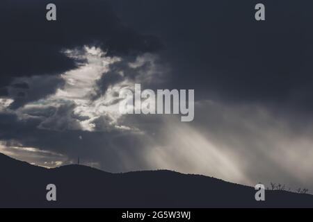 Dicke, stürmische Wolken über den Bergen mit intensiven Sonnenstrahlen, die durch die Berge ragen, und kontrastreicher Lichteinstrahlung im Winter in Tasmanien, Australien Stockfoto