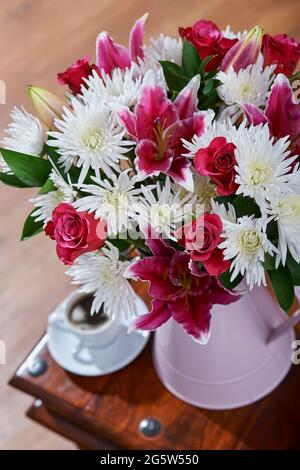 Ein Strauß rosa-weißer Blumen in einer pinkfarbenen Kannenvase mit schwarzem Kaffee auf einem Couchtisch in einer gemütlichen Atmosphäre Stockfoto