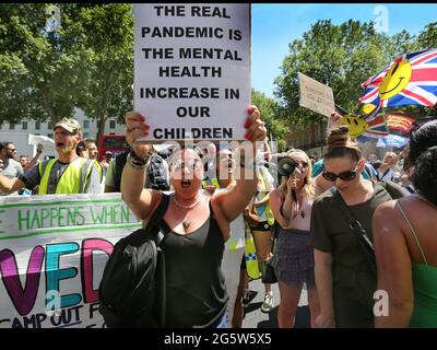 London, Großbritannien. Juni 2021. Ein Protestler hält ein Plakat hoch, auf dem die anhaltende Gefahr der Sperrung von Kindern hervorgehoben wird, während andere im Hintergrund Parolen singen.Demonstranten versammeln sich vor der Downing Street, um gegen Boris Johnsons Ankündigung einer Verlängerung der Sperrbestimmungen im Vereinigten Königreich zu protestieren, die ihrer Meinung nach auch ihre Menschenrechte verletzen Protest gegen das fortgesetzte Tragen von Masken und das Unterwerfen des Impfprogramms. Quelle: Martin Pope/SOPA Images/ZUMA Wire/Alamy Live News Stockfoto