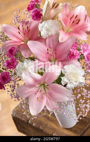 Eine Vase mit rosa asiatischen Lilien mit weißen und rosa Nelken und rosa Gypsophila auf einem Couchtisch in einem Raum Stockfoto