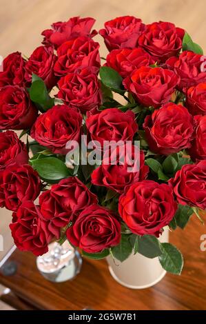 Zwei Dutzend rote valentinsrosen in einer Vase auf einem Couchtisch für besondere Anlässe wie den Valentinstag Stockfoto
