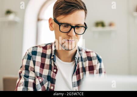 Junger lächelnder Geschäftsmann, benutzt Laptop, Mann arbeitet im Internet sitzt an einem Tisch mit einem modernen Laptop-Computer in einem Café vor dem Hintergrund o Stockfoto