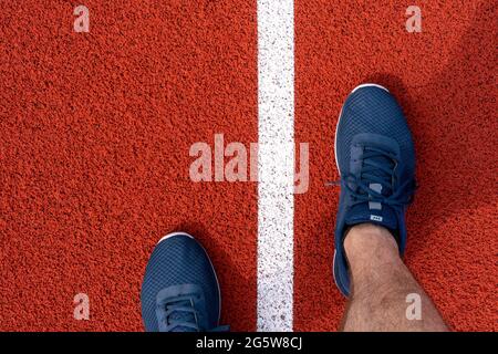 Ein Mann in Laufschuhen steht im Stadion auf der Strecke. Der Athlet bereitet sich auf den Wettkampf vor. Stockfoto