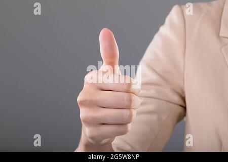 Mittelteil der kaukasischen Geschäftsfrau berührt virtuelle Schnittstelle auf grauem Hintergrund Stockfoto