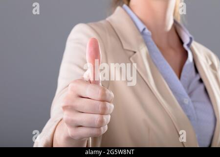 Mittelteil der kaukasischen Geschäftsfrau berührt virtuelle Schnittstelle auf grauem Hintergrund Stockfoto