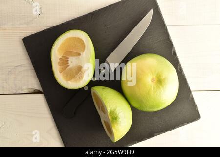 Zwei Hälften und eine ganz natürliche Citrus Sweetie auf einem Schiefertafel mit einem Metallmesser, Nahaufnahme, auf einem weißen Holztisch, Draufsicht. Stockfoto
