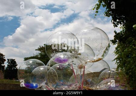 Transparente Luftballons dahinter, blauer Himmel, weiße Wolken, grüne Bäume Stockfoto