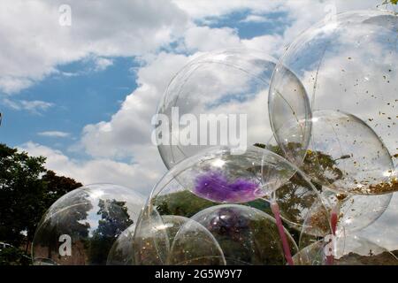 Transparente Luftballons dahinter, blauer Himmel, weiße Wolken, grüne Bäume Stockfoto