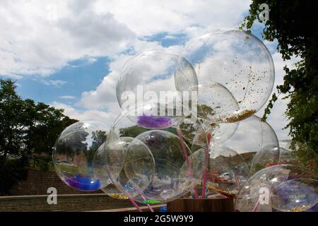 Transparente Luftballons dahinter, blauer Himmel, weiße Wolken, grüne Bäume Stockfoto