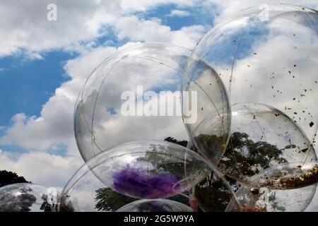 Transparente Luftballons dahinter, blauer Himmel, weiße Wolken, grüne Bäume Stockfoto