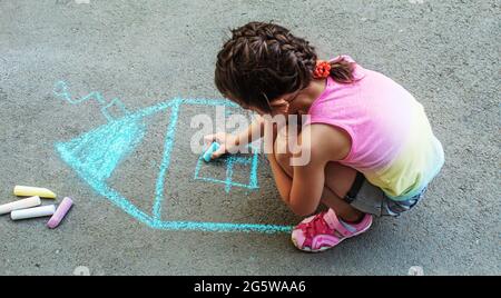 Das Kind zieht das Haus mit Kreide auf den Asphalt. Selektive konzentrieren. zeichnen. Stockfoto