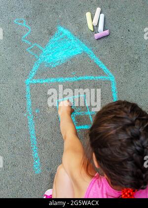 Das Kind zieht das Haus mit Kreide auf den Asphalt. Selektive konzentrieren. zeichnen. Stockfoto