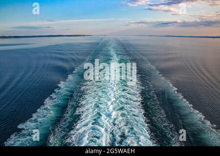 Wake von einem Schiff über den Ozean, während Sie die Ostsee segeln, an einem schönen Tag. Violettes und blaues Licht, das sich über das Meer und die Wellen reflektiert. Stockfoto