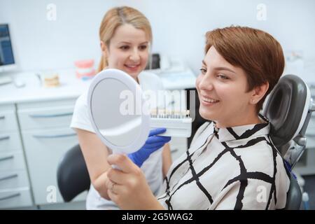 Glückliche junge Frau, die nach Zahnaufhellung die Zähne im Spiegel überprüft Stockfoto