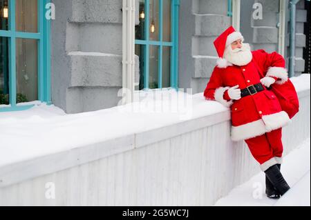 Der nachdenkliche weihnachtsmann lehnt sich im Winter an die Fassade eines Hauses Stockfoto