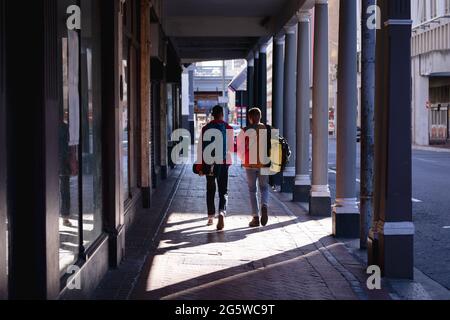 Rückansicht von zwei männlichen Freunden, die Rucksäcke tragen, die in einer umsäumten Stadtstraße spazieren gehen Stockfoto