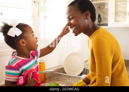 Lächelnde afroamerikanische Mutter und Tochter, die Spaß in der Küche haben, sich zusammen zu waschen Stockfoto